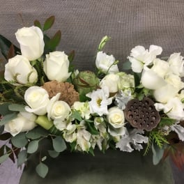 White roses and white blooms arranged with greenery in a low centerpiece
