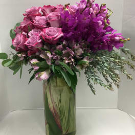 Pink roses and purple orchids arranged in a tall glass vase