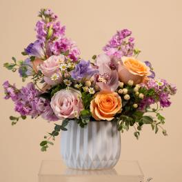 Pastel floral arrangement in a white vase with pink, purple, and peach blooms