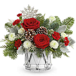 Red roses and white flowers in a clear glass vase with pinecones