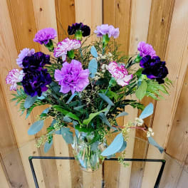 Tall clear vase of purple and lavender carnations with white-edged blooms and mixed foliage