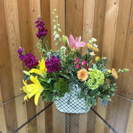 Colorful mixed flower arrangement in a white patterned ceramic container.