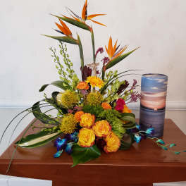 Tropical floral arrangement with orange birds of paradise and roses beside a tall candle