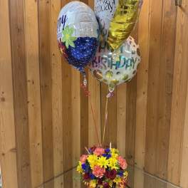 Birthday balloons above a colorful mixed flower arrangement in a vase