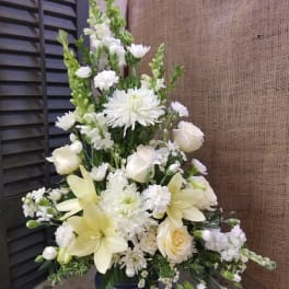 Tall white floral arrangement in a dark vase with lilies and roses
