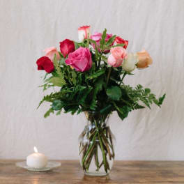 Mixed roses in a clear glass vase beside a small candle.