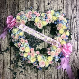 Heart-shaped floral wreath with pink and yellow roses and a pink ribbon