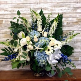 Blue hydrangeas and white flowers in a vase with a white ribbon