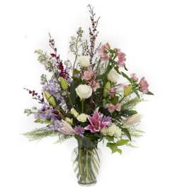 Tall mixed arrangement of pink lilies, white roses, and lavender blooms in a clear glass vase