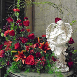 Red and orange floral arrangement beside a white angel statue