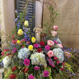 Large mixed floral arrangement with roses, hydrangeas, and an angel figurine