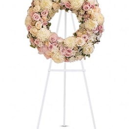 Round floral wreath of pale pink and cream roses on a white stand