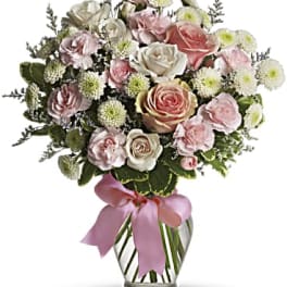 Pink and white rose bouquet in a clear glass vase with a pink ribbon
