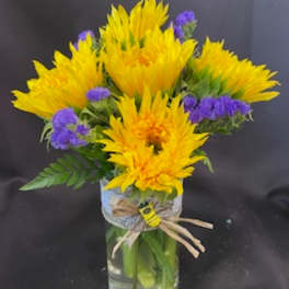Yellow flowers and purple filler in a clear glass vase
