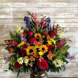 Large mixed flower arrangement in a gold vase with red, yellow, pink, and purple blooms