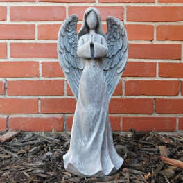 Gray angel statue with folded hands against a brick wall