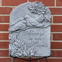 Gray memorial plaque with two birds and floral reliefs against a brick wall