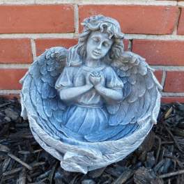Gray angel statue holding a rose in front of a brick wall