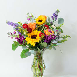 Mixed bouquet of sunflowers, roses, and purple flowers in a glass vase
