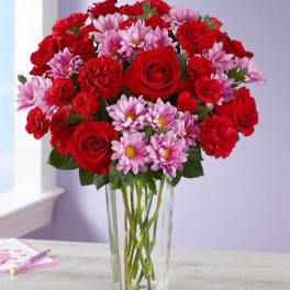 Bouquet of red roses and pink daisies in a clear glass vase