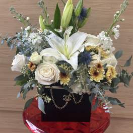 White lilies and roses arranged in a red vase with greenery