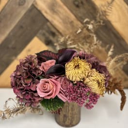 Bouquet of pink roses, purple hydrangea, and yellow chrysanthemums in a wooden vase