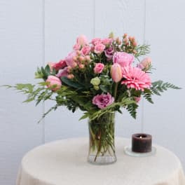 Pink mixed bouquet in a clear glass vase beside a small candle