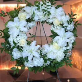 White floral wreath on a stand with lilies, roses, and hydrangeas