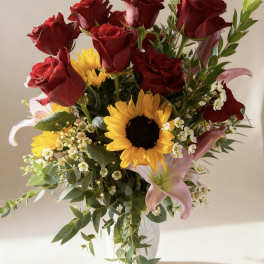 Bouquet of red roses, sunflowers, and pink lilies in a clear vase