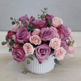 Low arrangement of mauve and light pink roses in a white ribbed ceramic vase