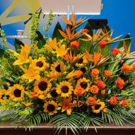 Large yellow and orange altar-style flower arrangement with sunflowers, lilies, roses, and birds of paradise.
