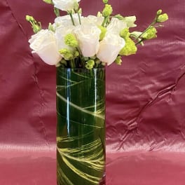 White roses and green buds arranged in a tall glass vase.
