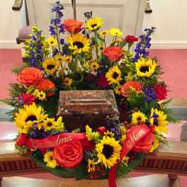 Colorful floral wreath around a memorial urn with red ribbons