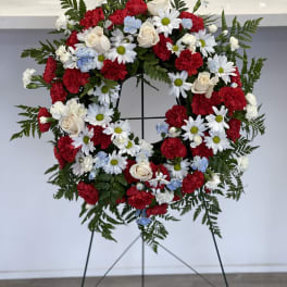 Circular funeral wreath with red, white, and blue flowers on a stand
