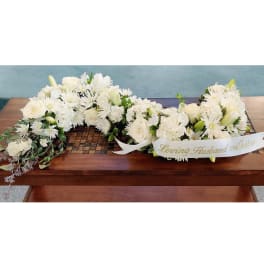 White funeral floral arrangement with a ribbon on a wooden table