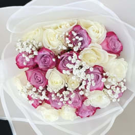 Bouquet of white and pink roses with small white filler flowers wrapped in sheer white paper