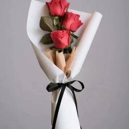 Three red roses wrapped in white paper with a black ribbon