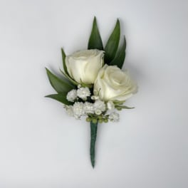 White rose boutonniere with small white filler flowers and green leaves
