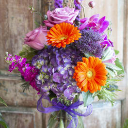 Bouquet of pink roses, orange gerberas, and purple flowers in a glass vase