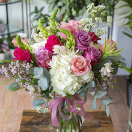 Pink and white rose bouquet in a glass vase with a ribbon