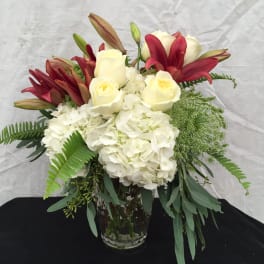 White hydrangeas with ivory roses and red lilies in a clear glass vase
