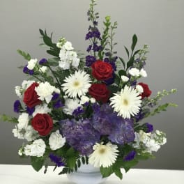 Red roses, white gerberas, and purple hydrangeas in a white vase