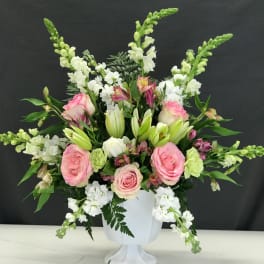 Pink roses and white lilies arranged in a white pedestal vase