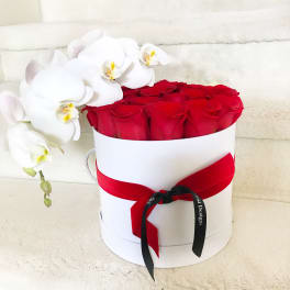 Red roses in a white hat box with white orchids draped over the side