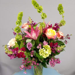 Mixed bouquet with roses, lilies, and purple blooms in a glass vase