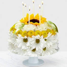 Sunflower and white daisy cake with lit candles on a pedestal stand