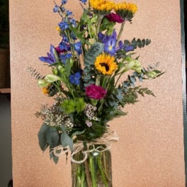 Tall mixed bouquet in a glass vase with blue, yellow, and magenta flowers