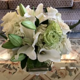 White lilies and pale green flowers in a square glass vase
