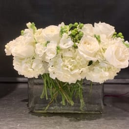 White roses and hydrangeas arranged in a clear rectangular vase