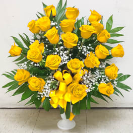 Yellow roses arranged in a white pedestal vase with baby's breath